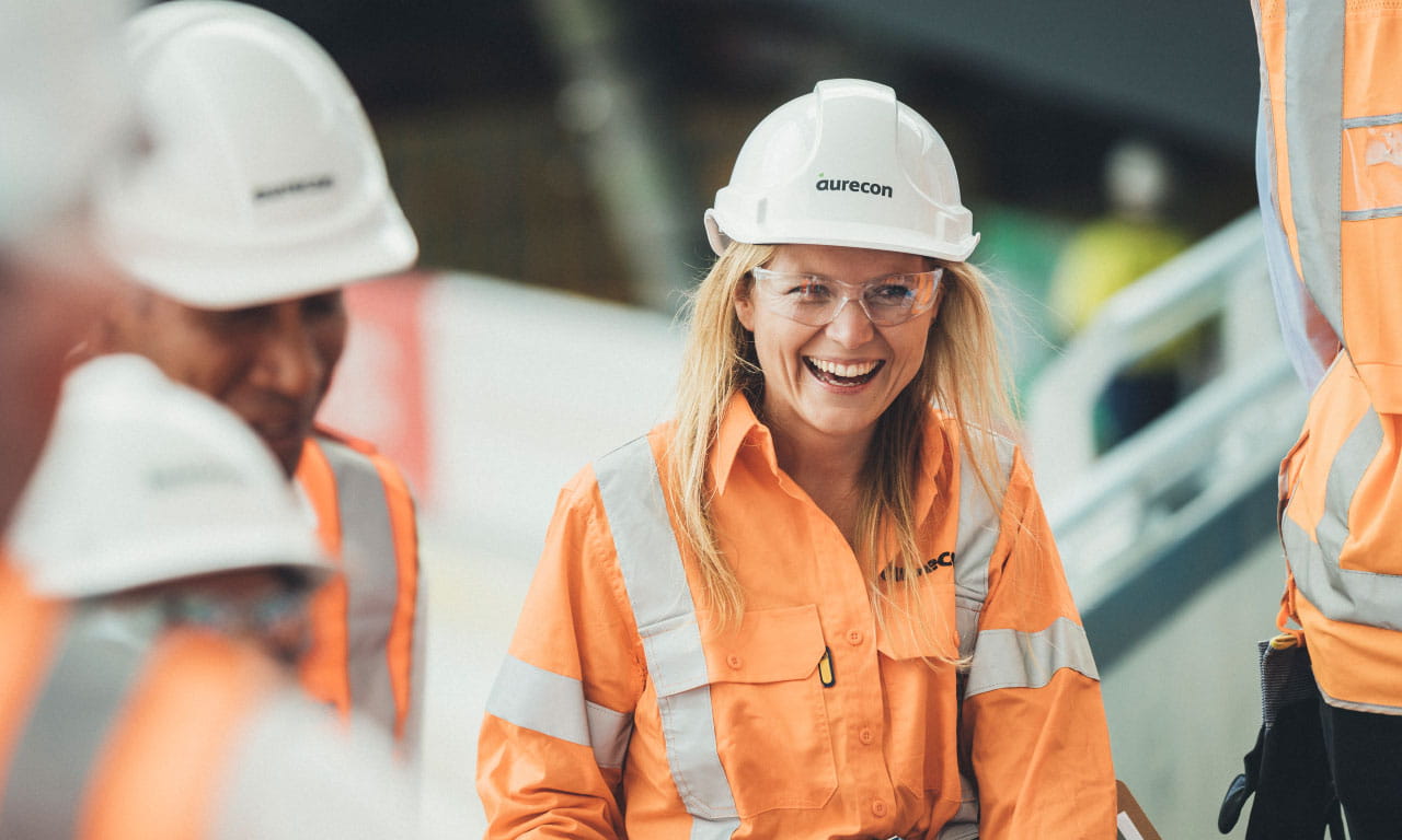 Woman engineer in hard hat working on construction site, smiling with team members