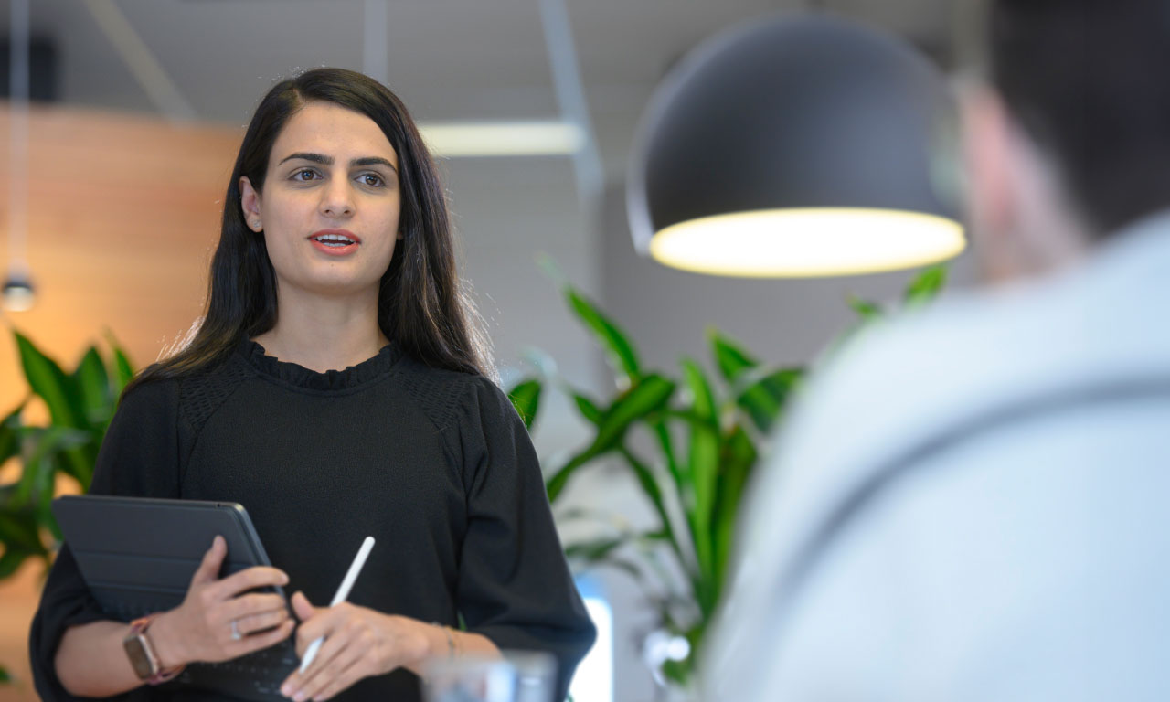 Woman holding tablet in conversation with man sitting down off screen