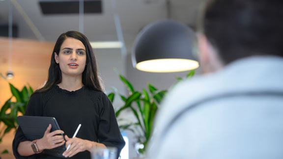 Woman holding tablet in conversation with man sitting down off screen