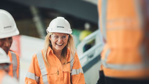Woman engineer in hard hat working on construction site, smiling with team members