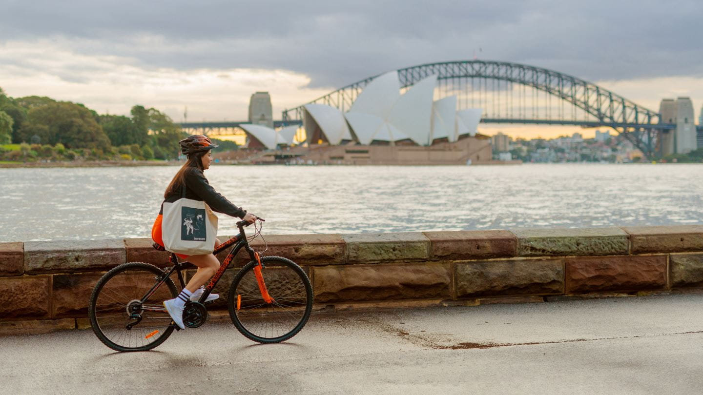 Aurecon's Juliana Fernandez riding her bike with backdrop of Sydney Harbour Bridge and Sydney Opera House.