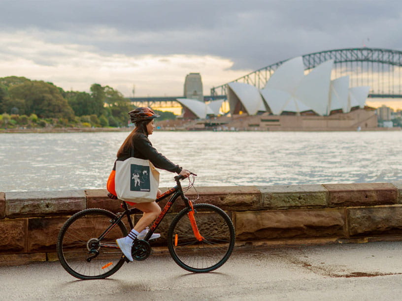 Aurecon's Juliana Fernandez riding her bike with backdrop of Sydney Harbour Bridge and Sydney Opera House.