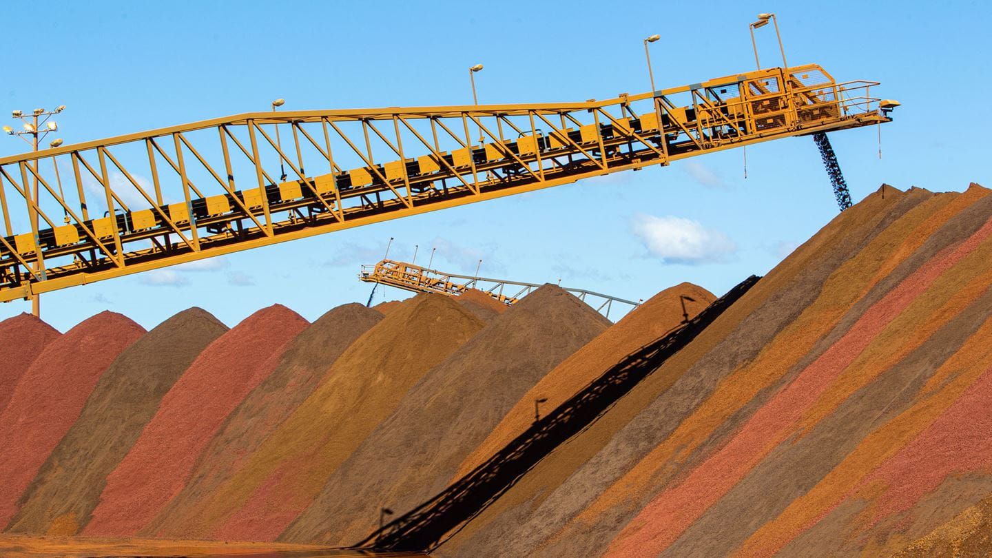 Large piles of iron ore at a mining facility, with conveyor belts used for transport and stacking.