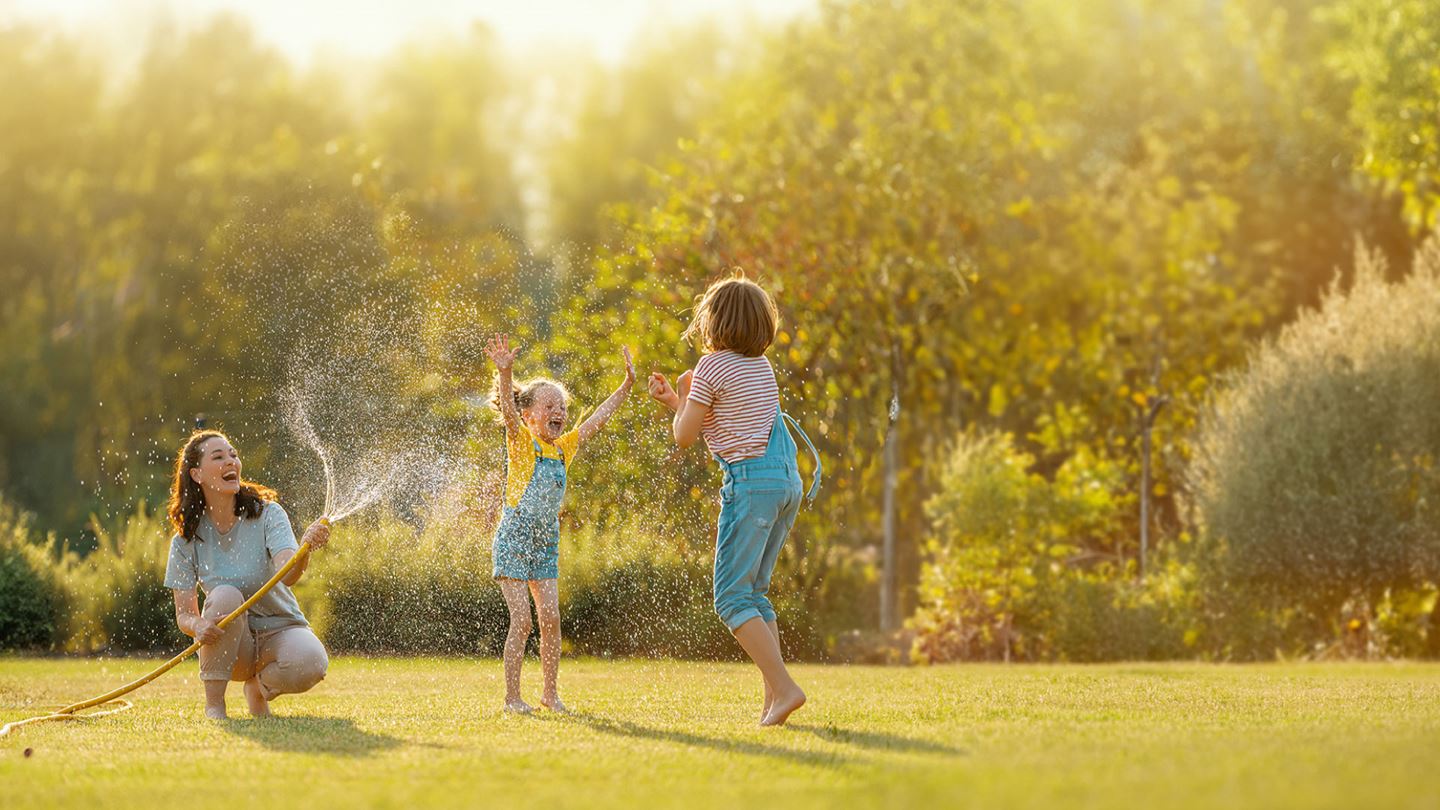 Woman and children playing with water from hose.