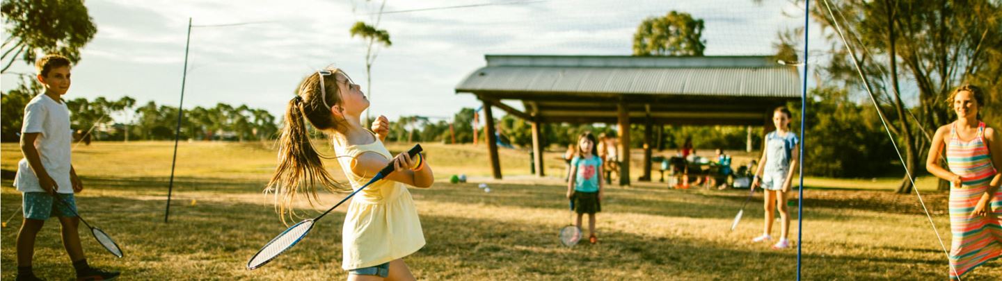 Young girl playing badminton with her family at park.