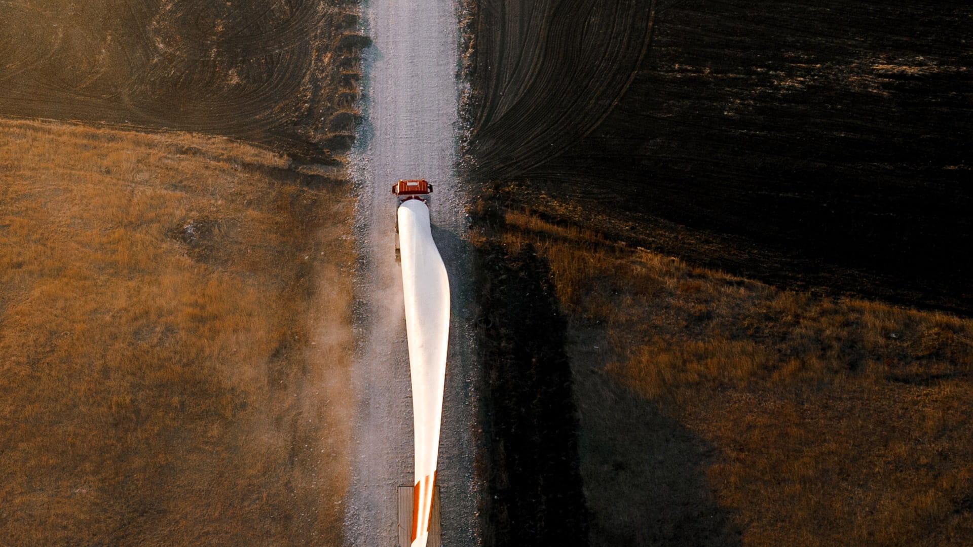 Wind turbine blade being transported by truck on a rural road.