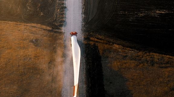 Wind turbine blade being transported by truck on a rural road.