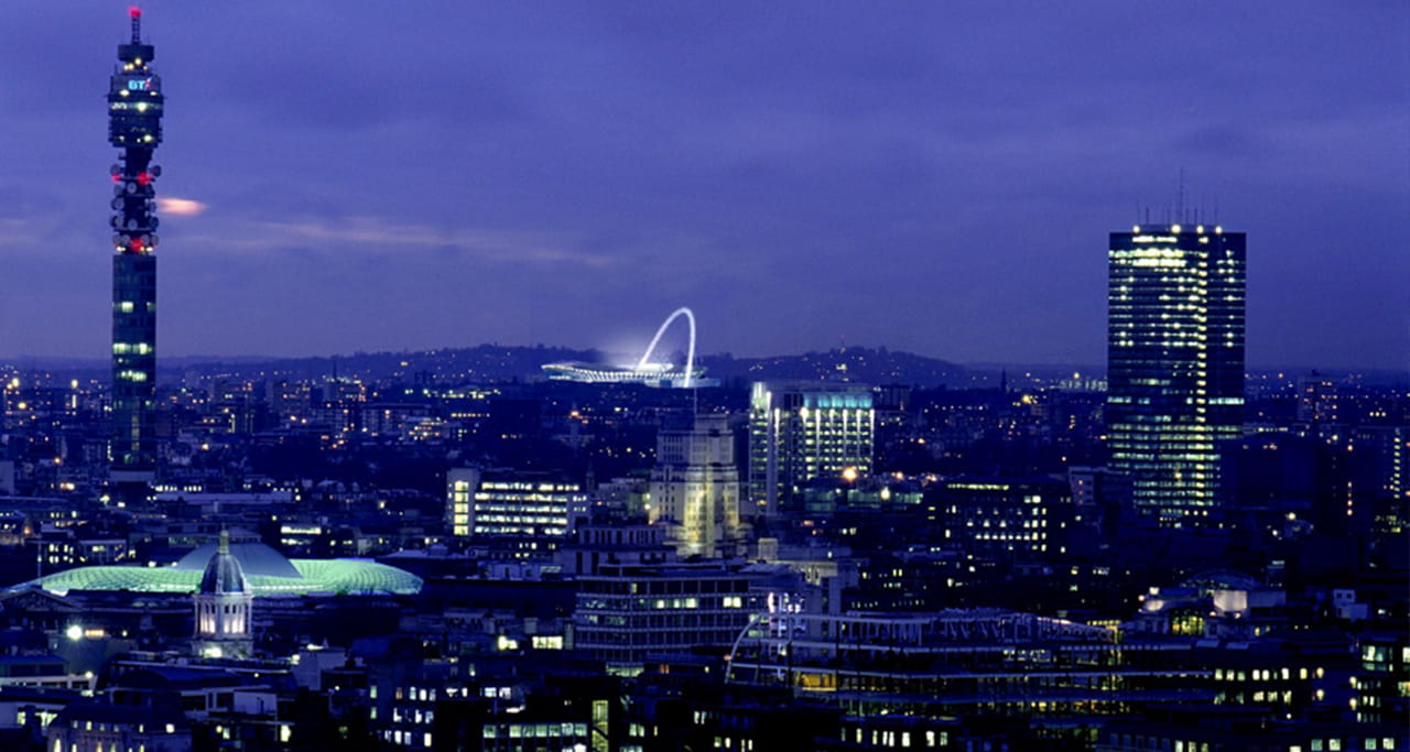 An aerial view of London with the Wembley Stadium Arch lit up in the background.