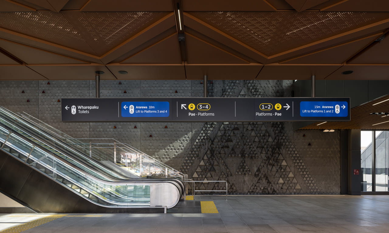 The interior of Maungawhau Station (also known as Mt Eden Station) features distinct architectural elements and modern directional signage pointing toward platforms and amenities.